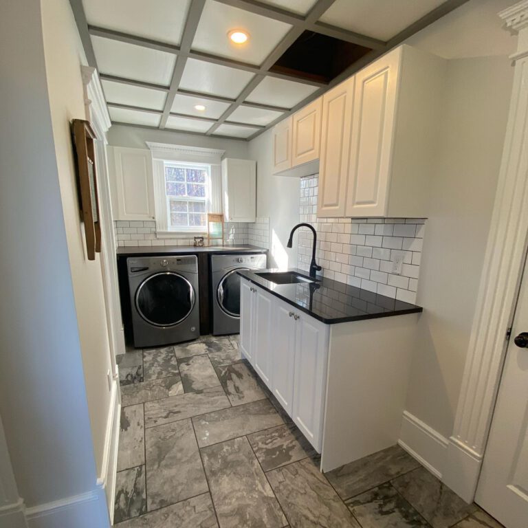 Laundry room with a front-load washer and dryer, white cabinets, a subway tile backsplash and a coffered ceiling