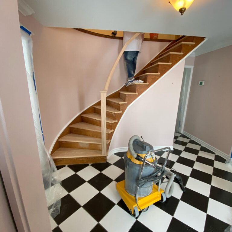 Curved staircase during a rebuild, with new unfinished oak treads above a black and white checkered tile floor