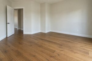 Empty renovated room with a clean warm oak hardwood floor, white baseboards and daylight from an open doorway
