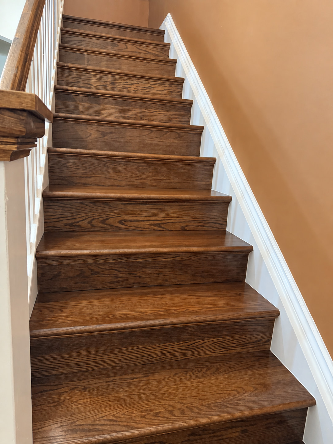 Oak staircase stained warm brown, with a wood handrail, white spindles and a white painted skirt board