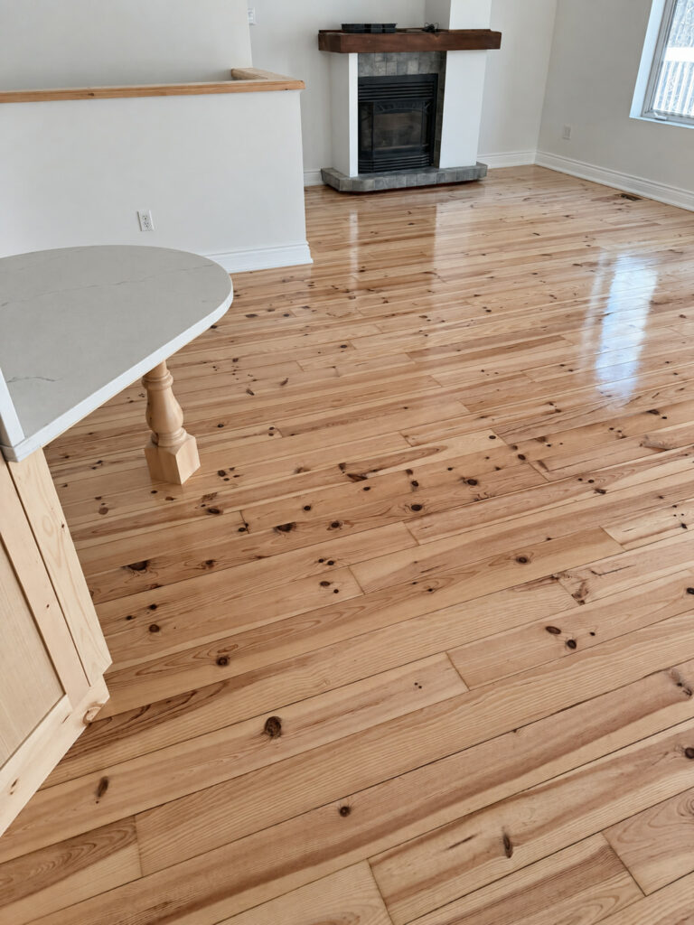 Glossy knotty pine floor in an open living area with a fireplace and a rounded white counter