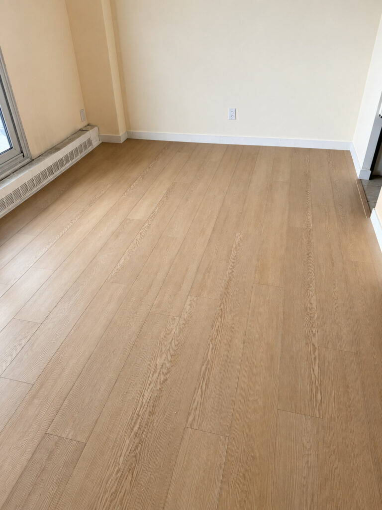 Light oak plank floor in an empty room with white baseboards and a baseboard heater