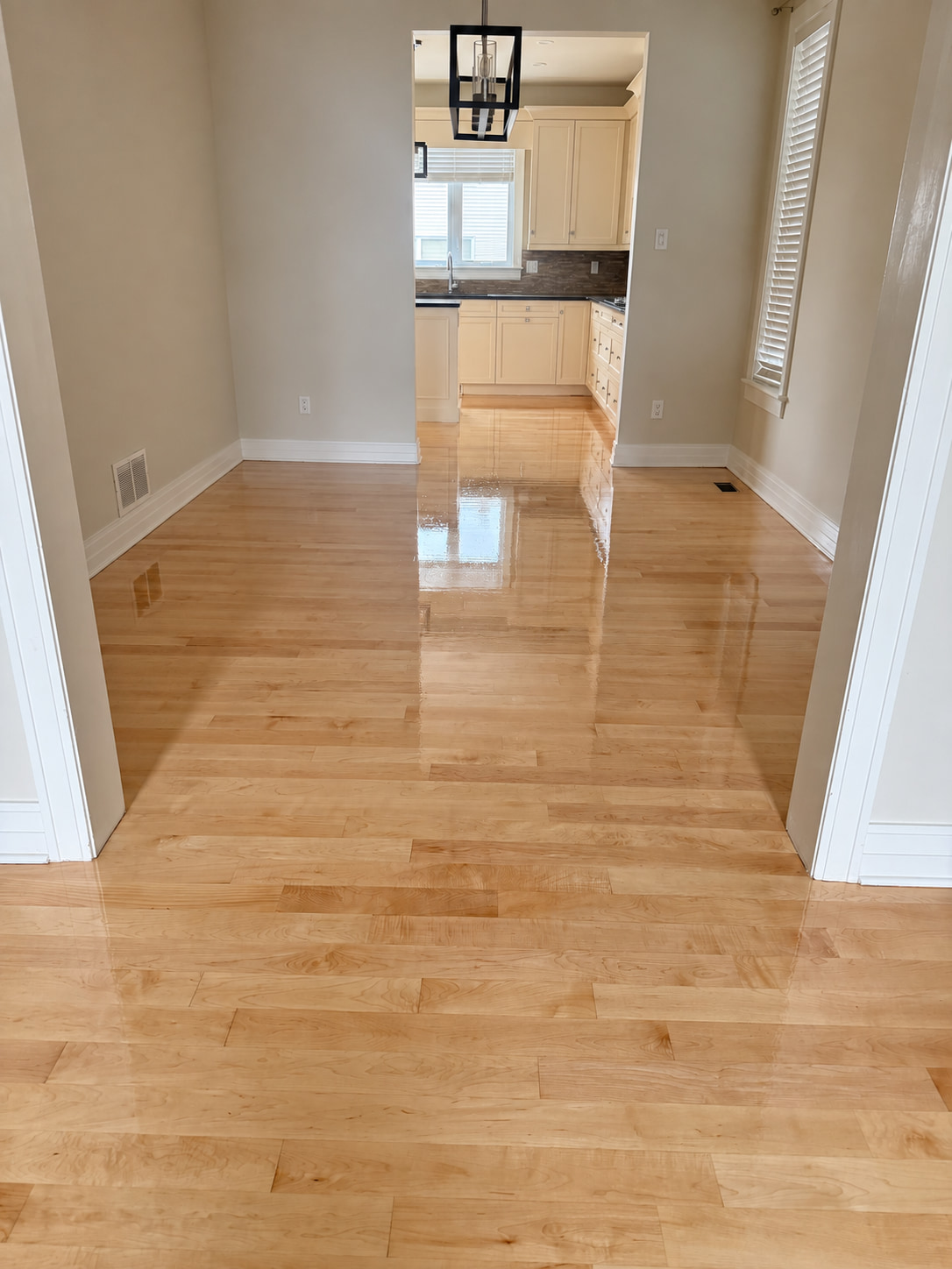 Glossy light hardwood floor running from a front hallway into a kitchen