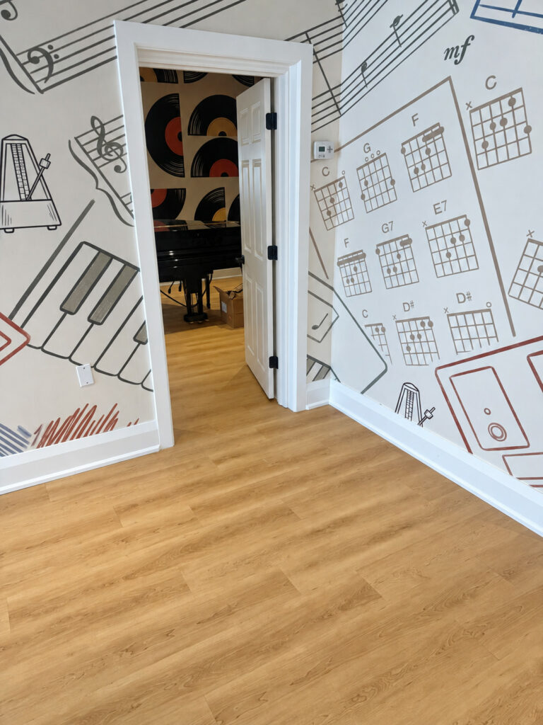 Wood look plank flooring at a music studio doorway beside a mural of piano keys and chord charts