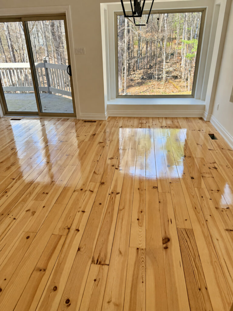 High gloss knotty pine floor reflecting daylight from a patio door and a large window