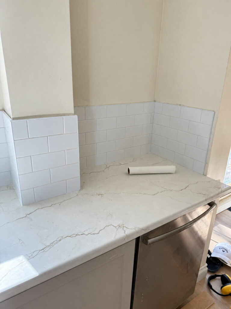 White subway tile backsplash wrapping a kitchen corner above a white quartz counter with grey veining