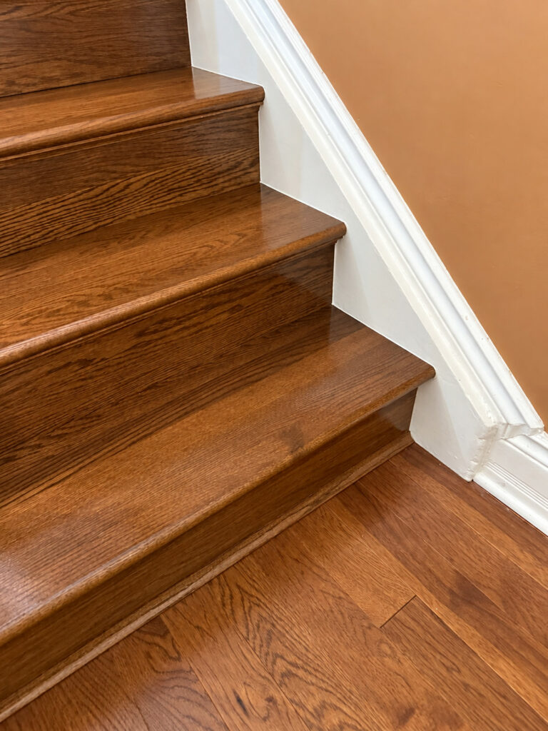 Close view of stained oak stair treads with rounded nosings beside a white painted skirt board