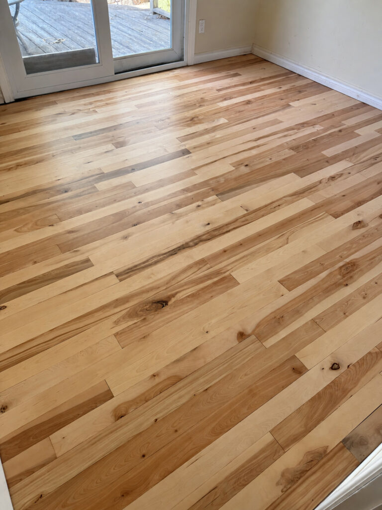 Natural hardwood with mixed light and dark boards in a room with patio doors to a deck
