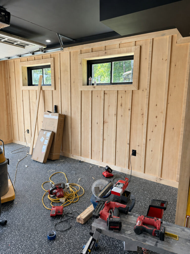 Garage conversion in progress, with vertical pine board panelling around two windows and tools on a flake floor