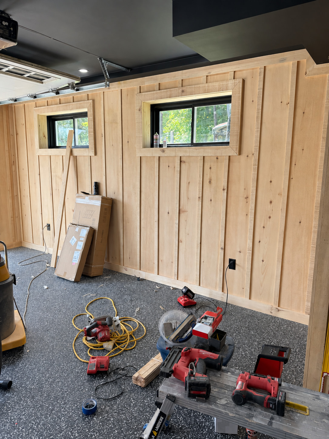 Garage conversion in progress, with vertical pine board panelling around two windows and tools on a flake floor