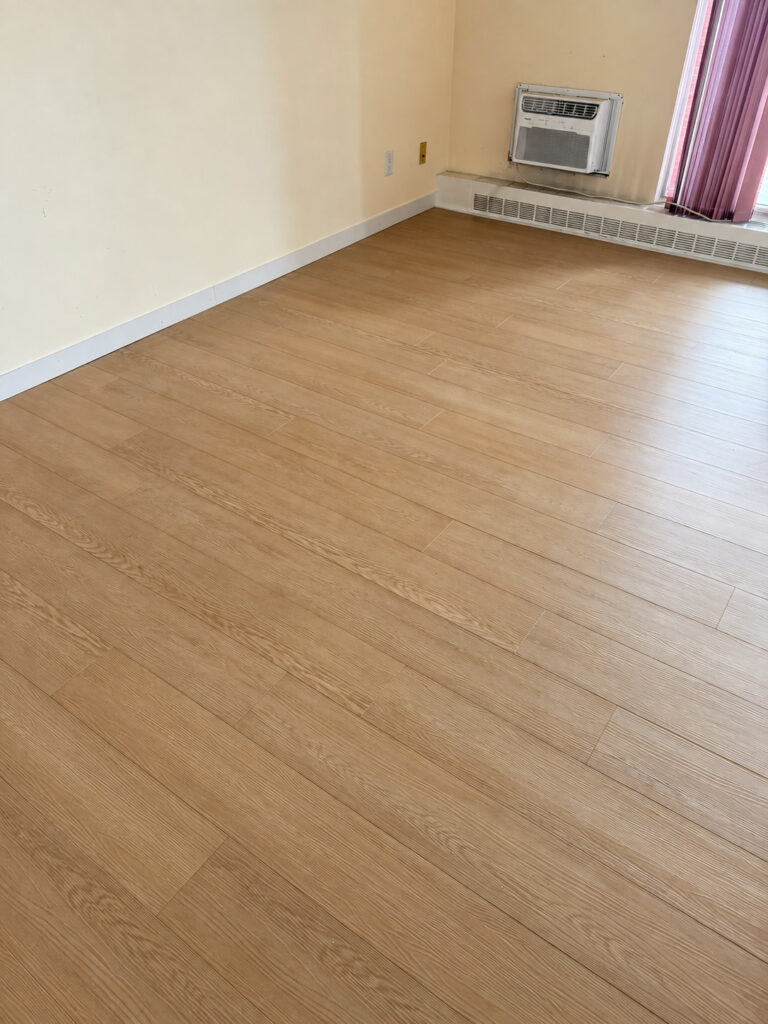 Warm toned plank floor in an empty room with white baseboards, a baseboard heater and a wall air conditioner