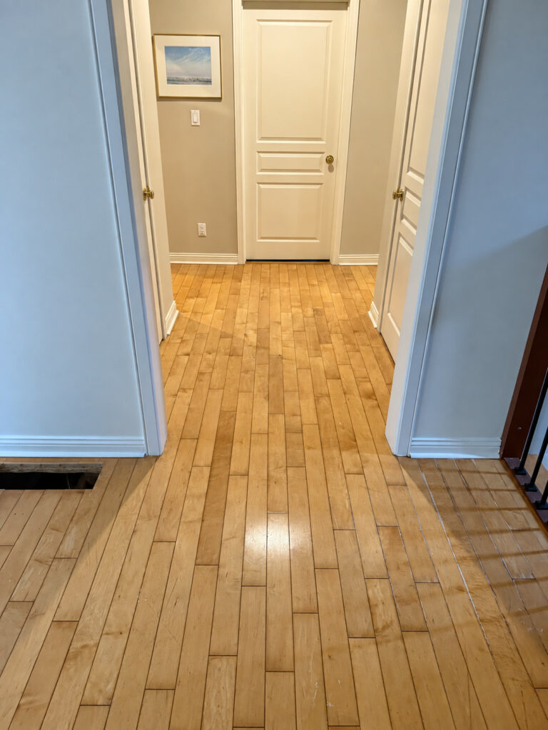 Glossy strip hardwood floor running down a hallway to a white panel door