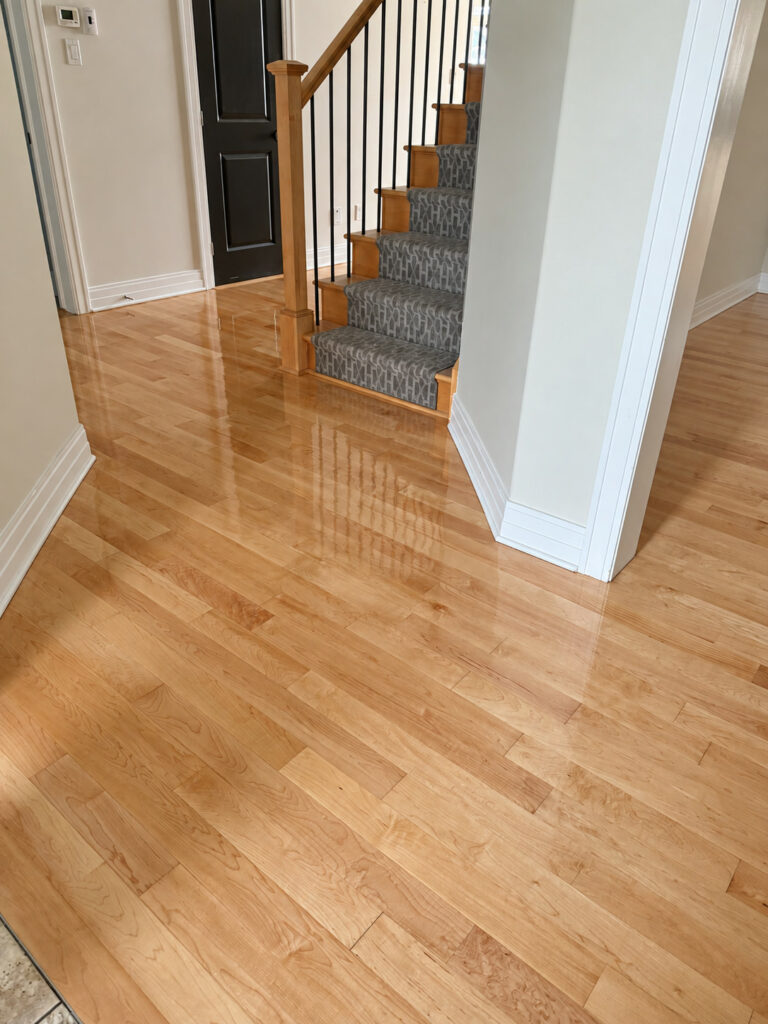 Glossy oak floor in a front entry around a staircase with a patterned carpet runner
