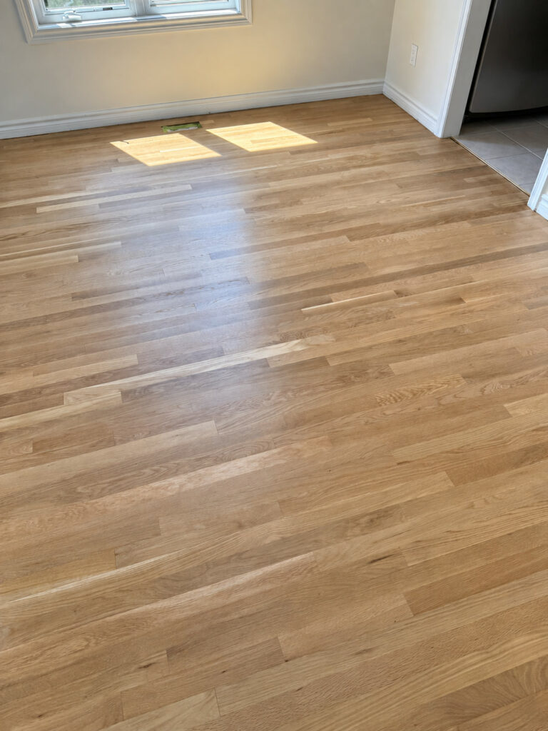 Oak strip floor in an empty room with patches of sunlight near the window