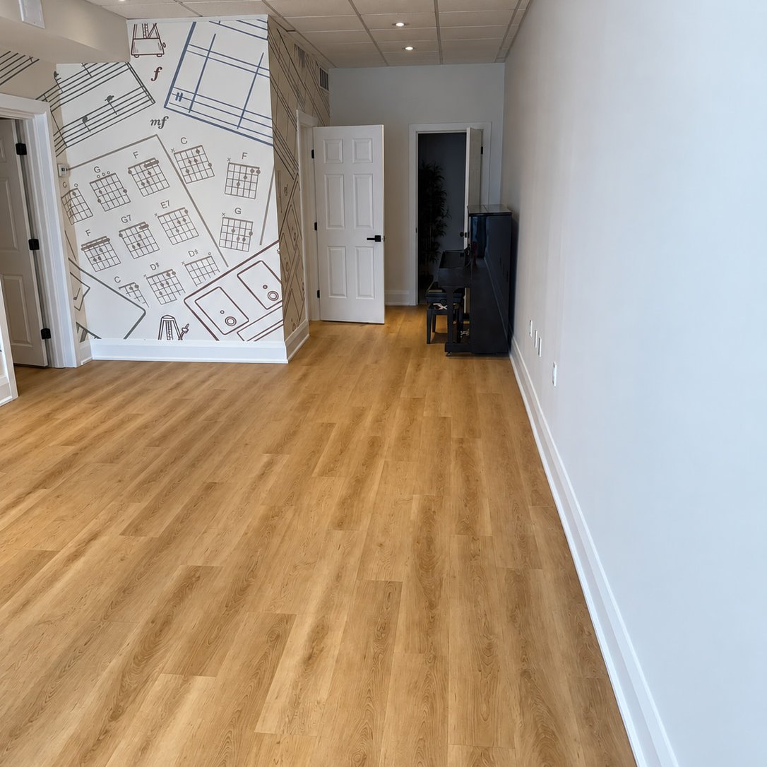 Long music studio room with wood look plank flooring, a chord chart mural and an upright piano