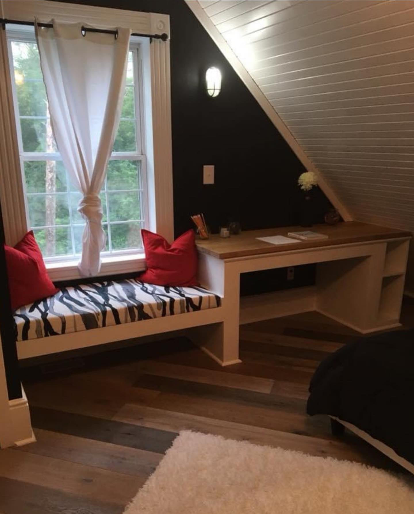 Bedroom with a built-in window seat and desk, a dark accent wall and a mixed-tone plank floor