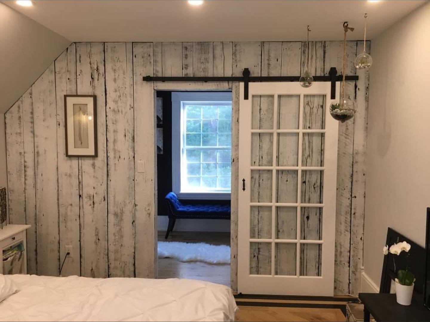 Bedroom with a whitewashed plank wall, a sliding glass barn door and a natural oak floor